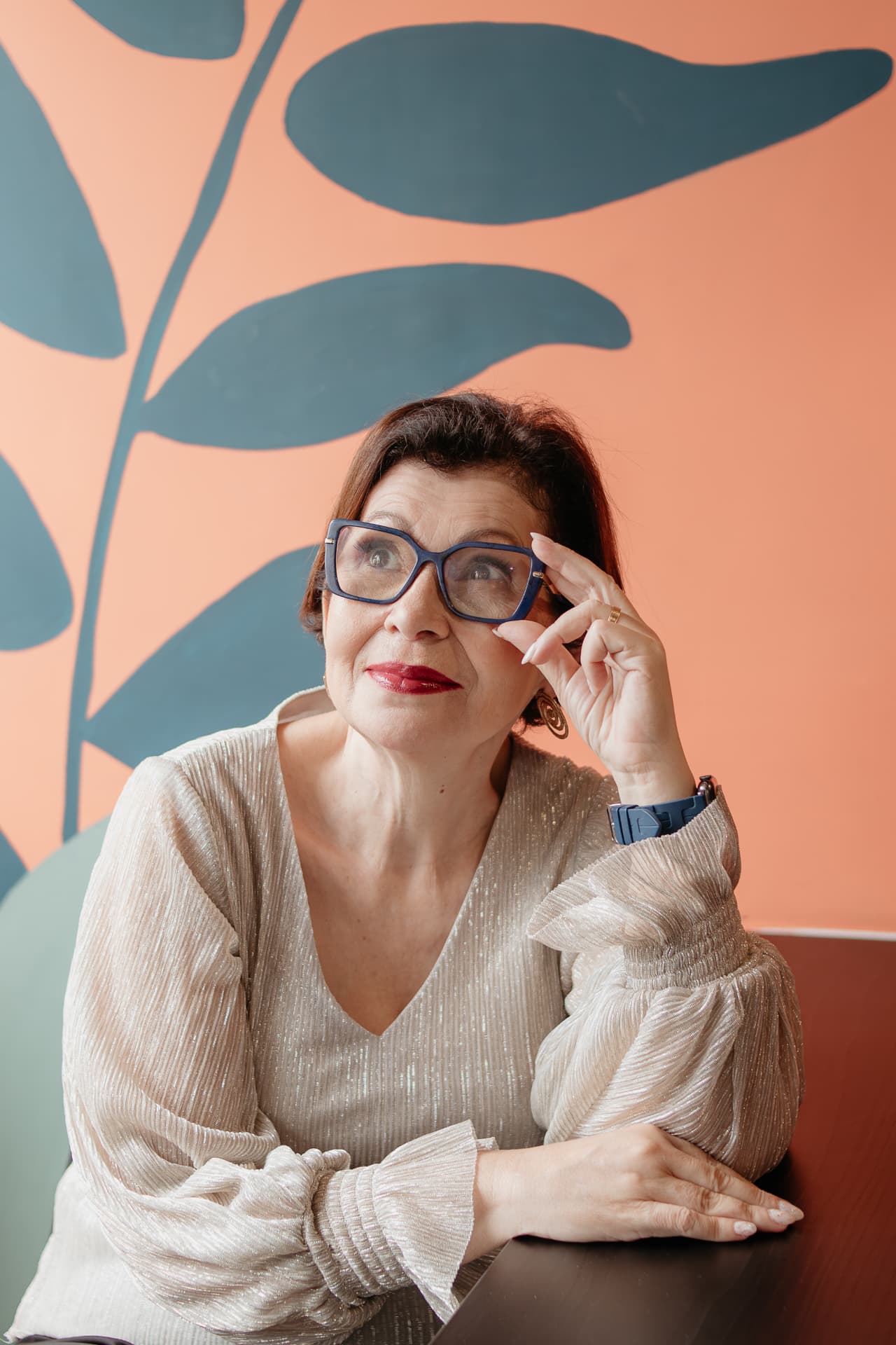 Retrato de Marizete Neves apoiada a uma mesa, em ambiente com mural artístico
