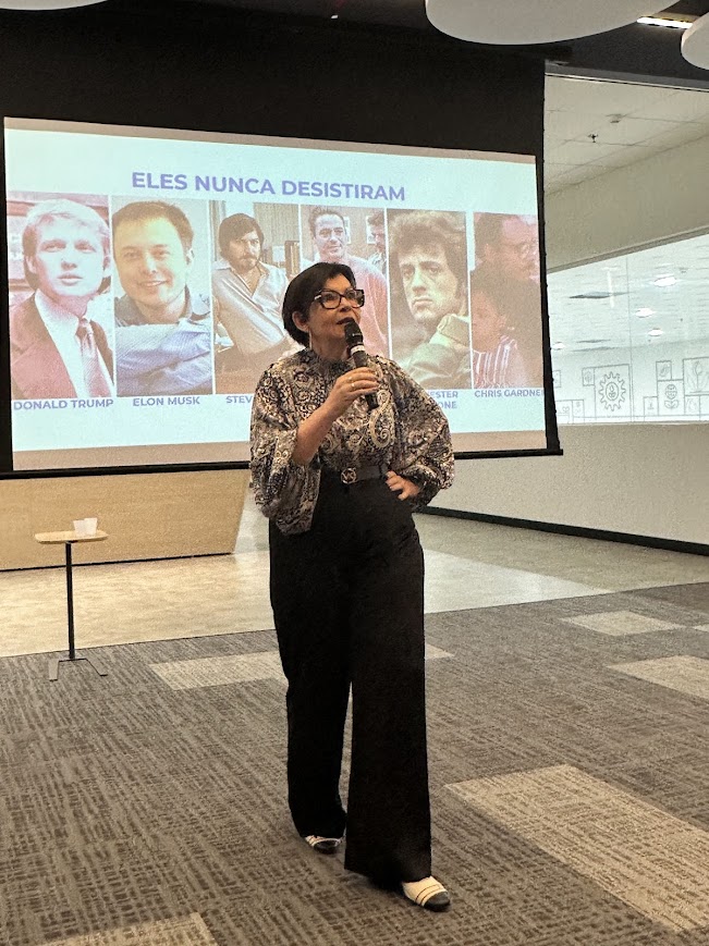 Marizete Neves apresentando conteúdo com microfone diante de um telão em evento